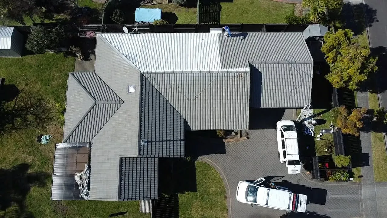 Aerial view of a tile roof midway through a repaint, the freshly coated section standing out against the faded original