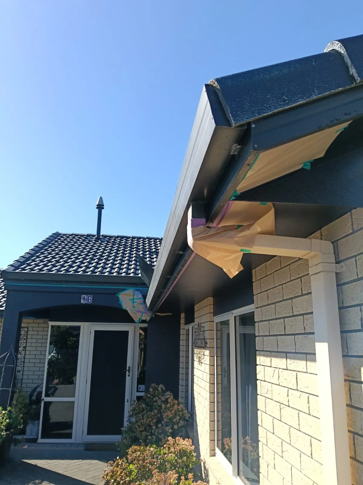 Eaves, spouting and brickwork masked with paper and tape below a freshly painted charcoal roof