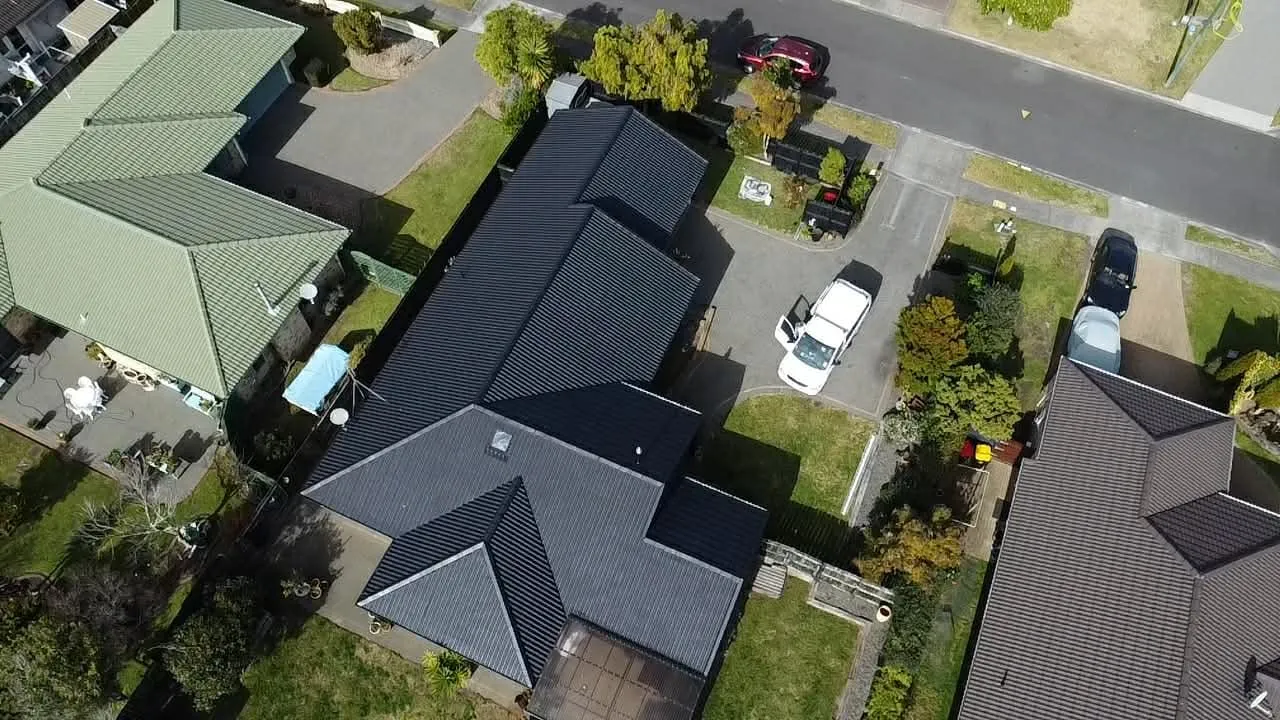 Aerial view of a finished charcoal tile roof on a suburban house, the work van parked in the driveway below