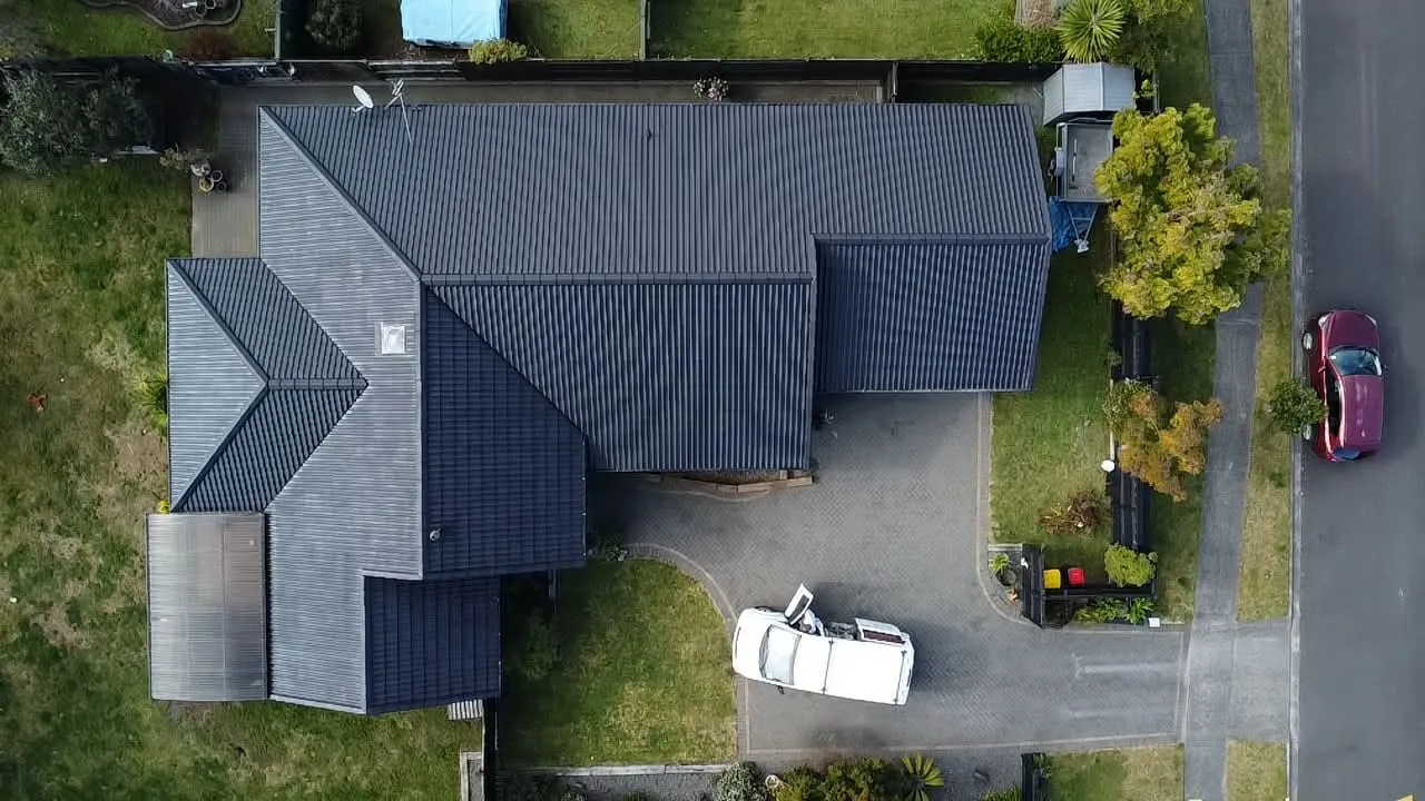 Drone view looking down on a repainted dark charcoal tile roof with a paved driveway and the work van alongside